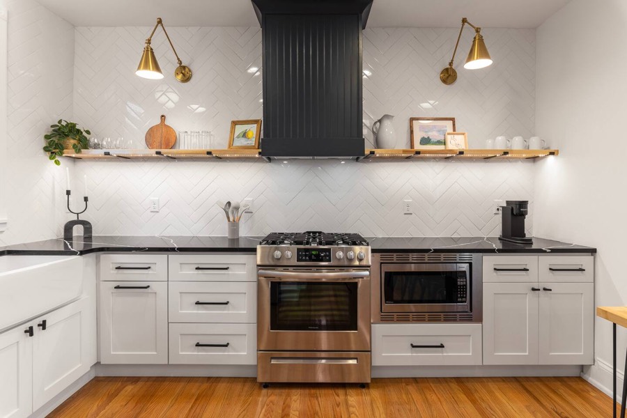 Downstairs kitchen with white cabinets, open shelving, brass sconces, and a gas range.