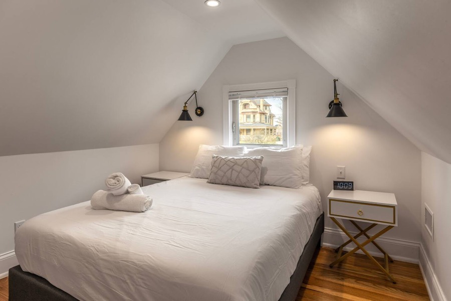 Top-floor bedroom tucked under the roofline, with a dormer window and wall sconces.