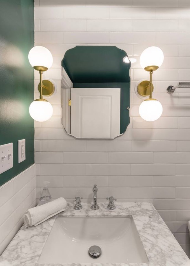 Bathroom with a marble top, brass and glass sconces, and a deep green accent wall.