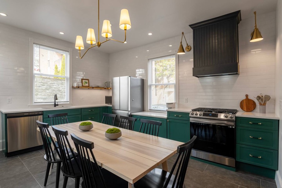 The upstairs kitchen — deep green cabinets, butcher-block counters, gas range, and a table that seats the group.