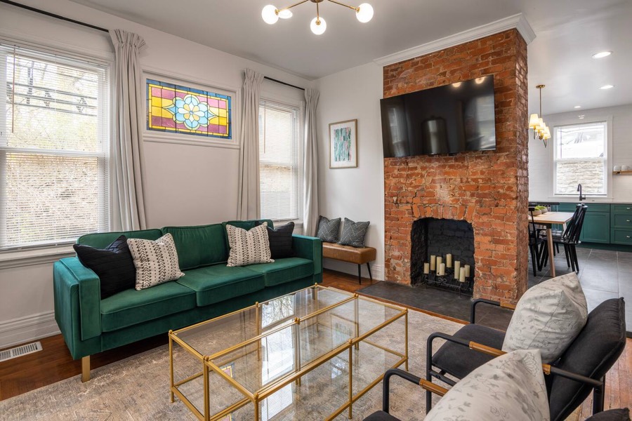 Living room with an exposed brick fireplace, green velvet sofa, and original stained glass.