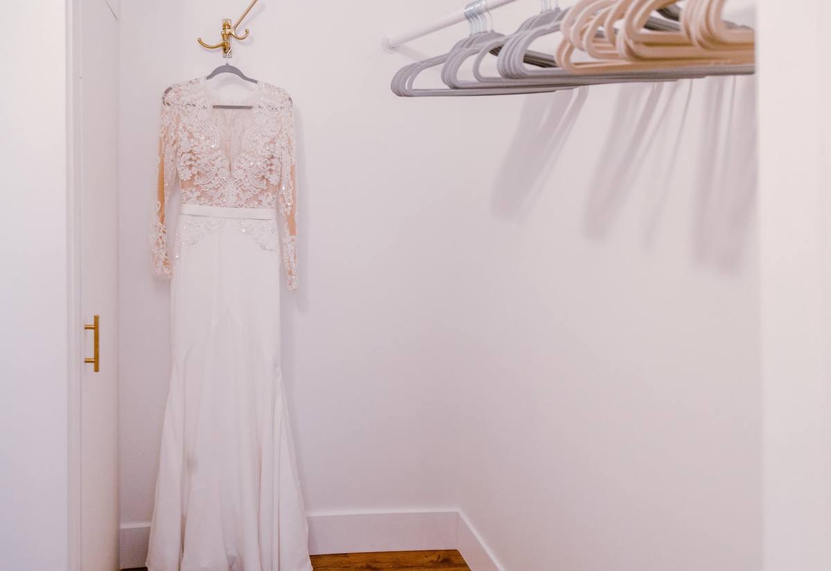 A lace wedding gown hanging in a walk-in closet in the three-unit building, beside a rail of empty hangers
